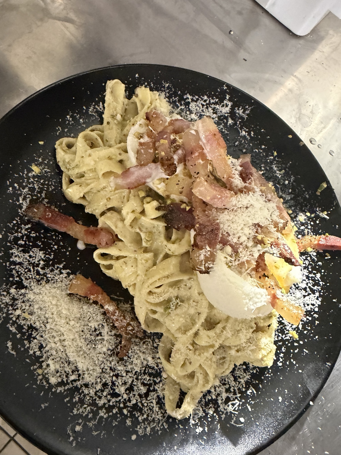 Pasta cremosa servita in piatto nero con burrata e pancetta