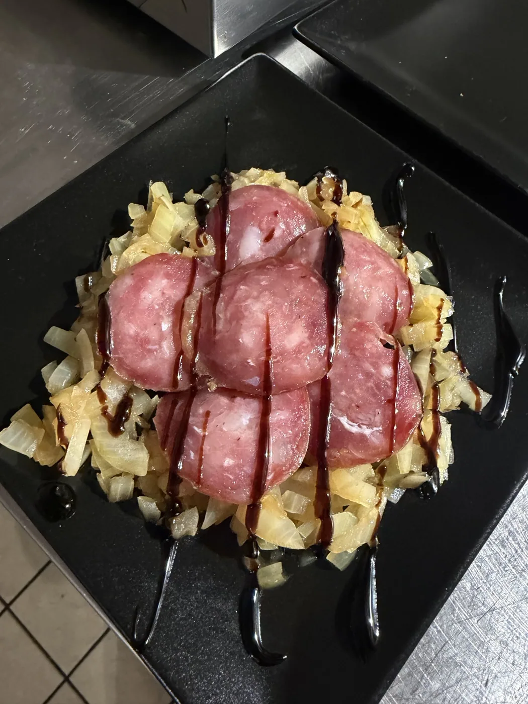 Salame all’aceto con cipolle caramellate su piatto nero
